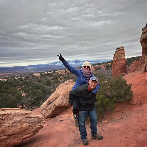 Michelle throws up a peace sign while sitting on her husband's back in front of a canyon